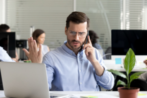 Distressed man sitting in front of laptop on the phone