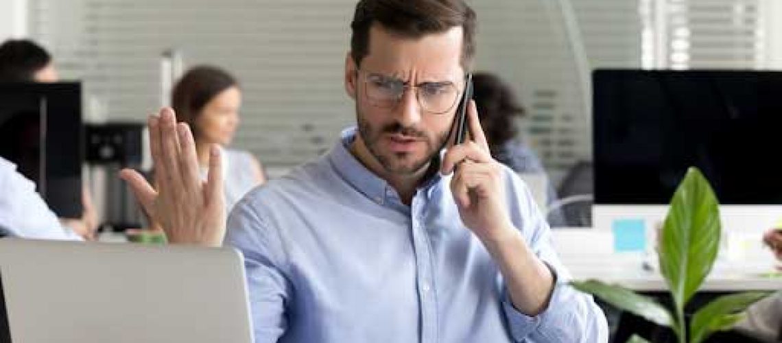 Distressed man sitting in front of laptop on the phone